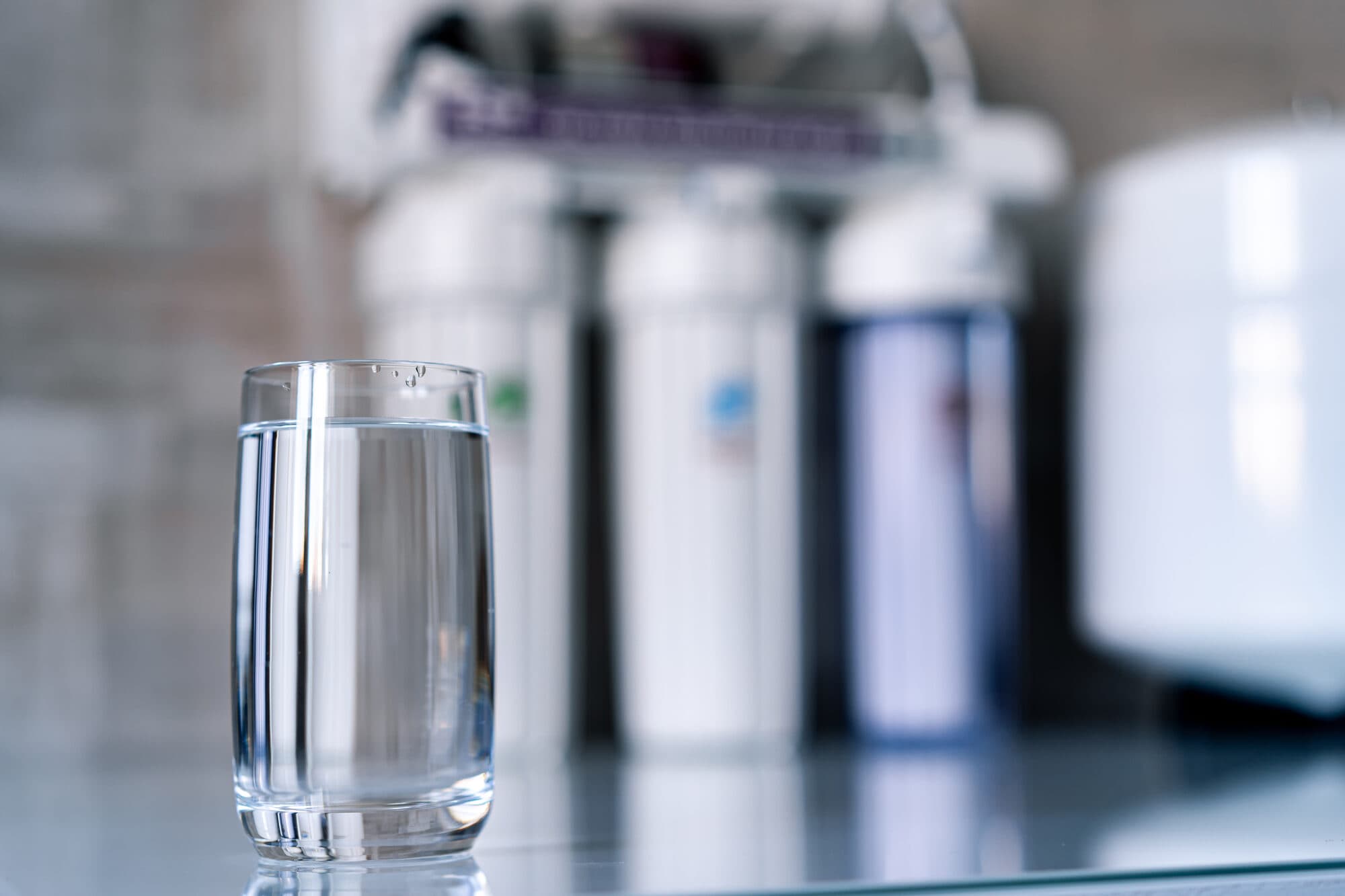 Under-sink reverse osmosis system beside a glass of filtered water
