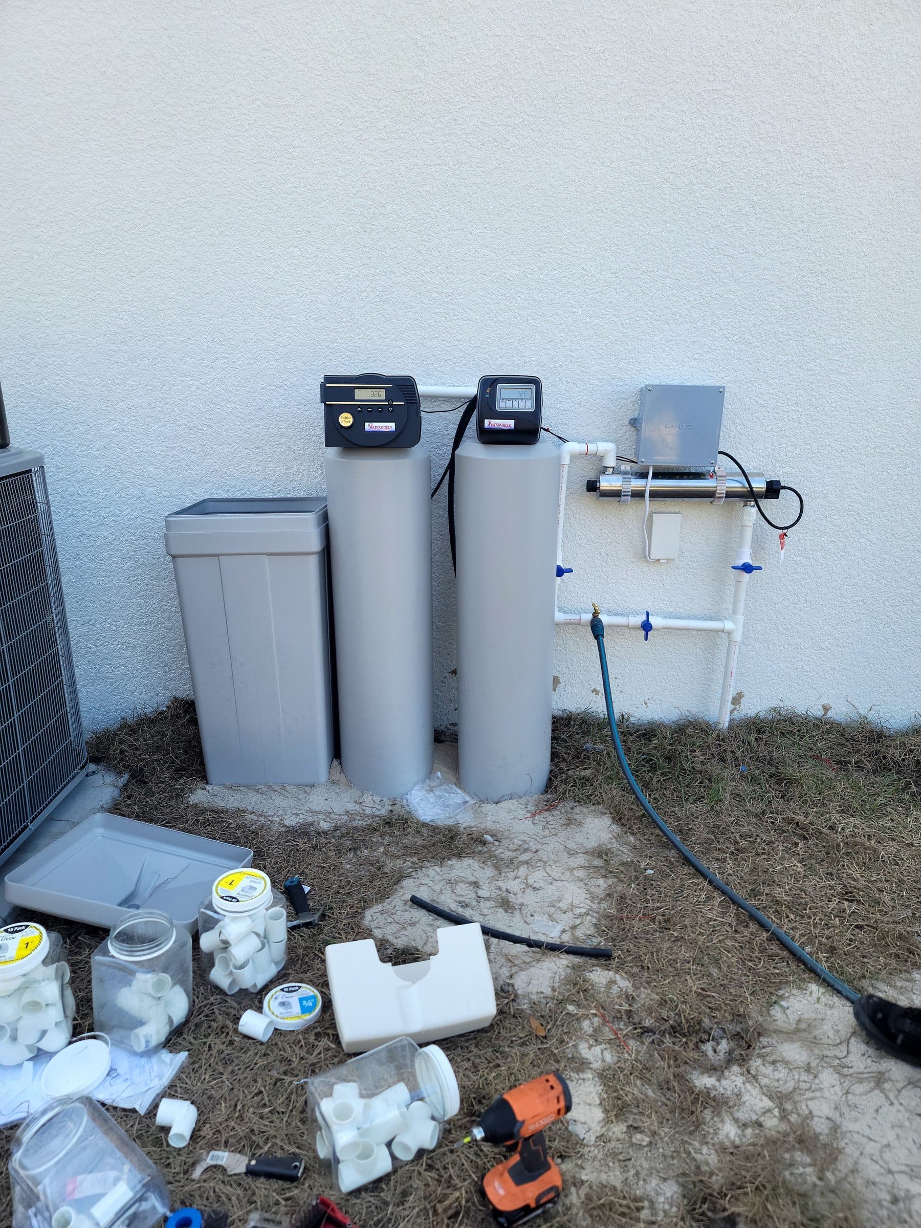 Twin softener tanks with UV disinfection installed against a home's exterior wall