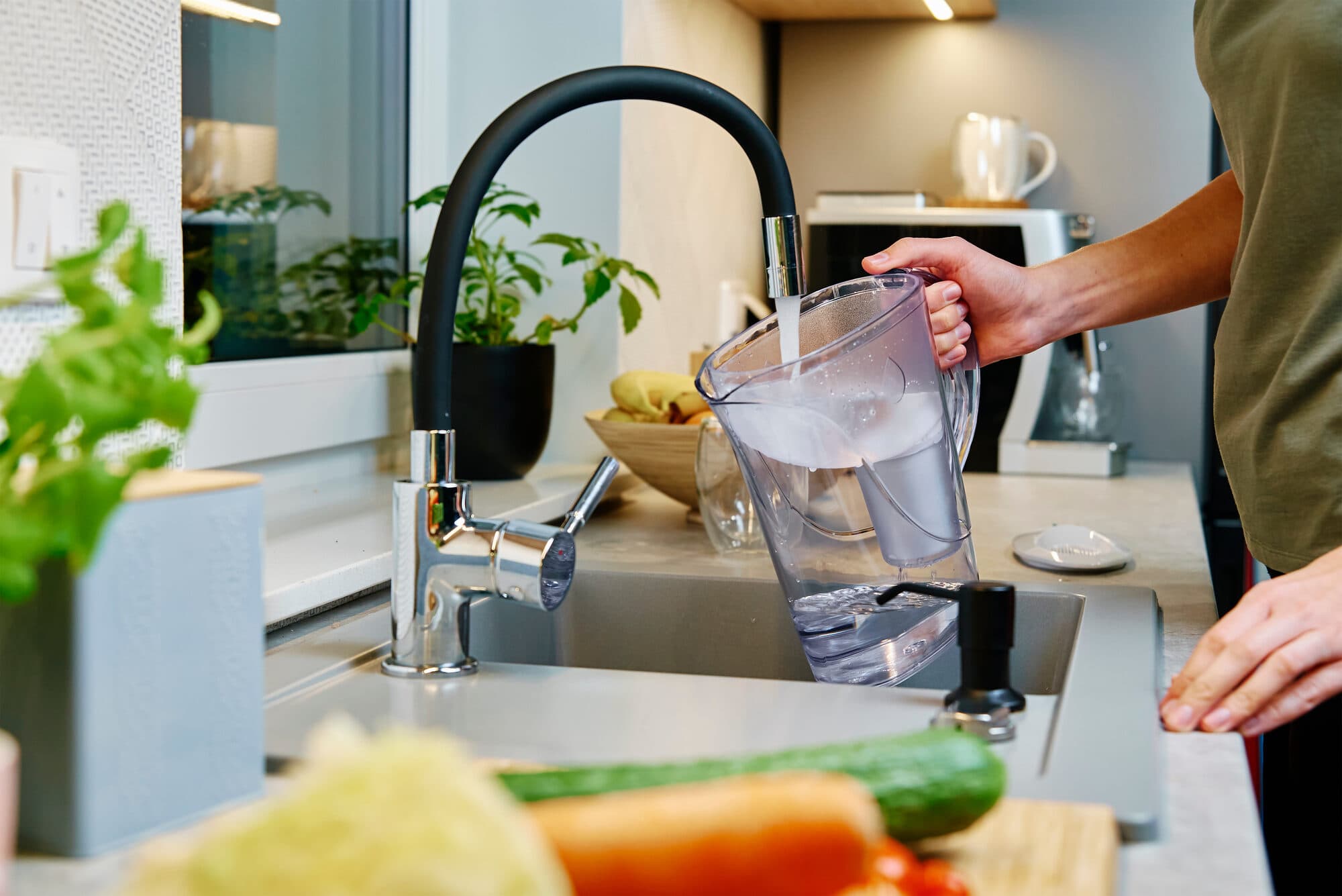 Filling a filter pitcher from a kitchen tap beside fresh vegetables