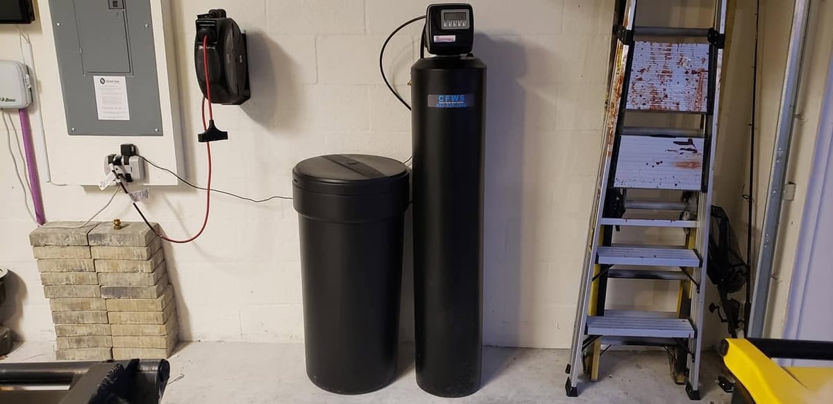Water softener and filtration system equipment installed against a wall with pipes and accessories